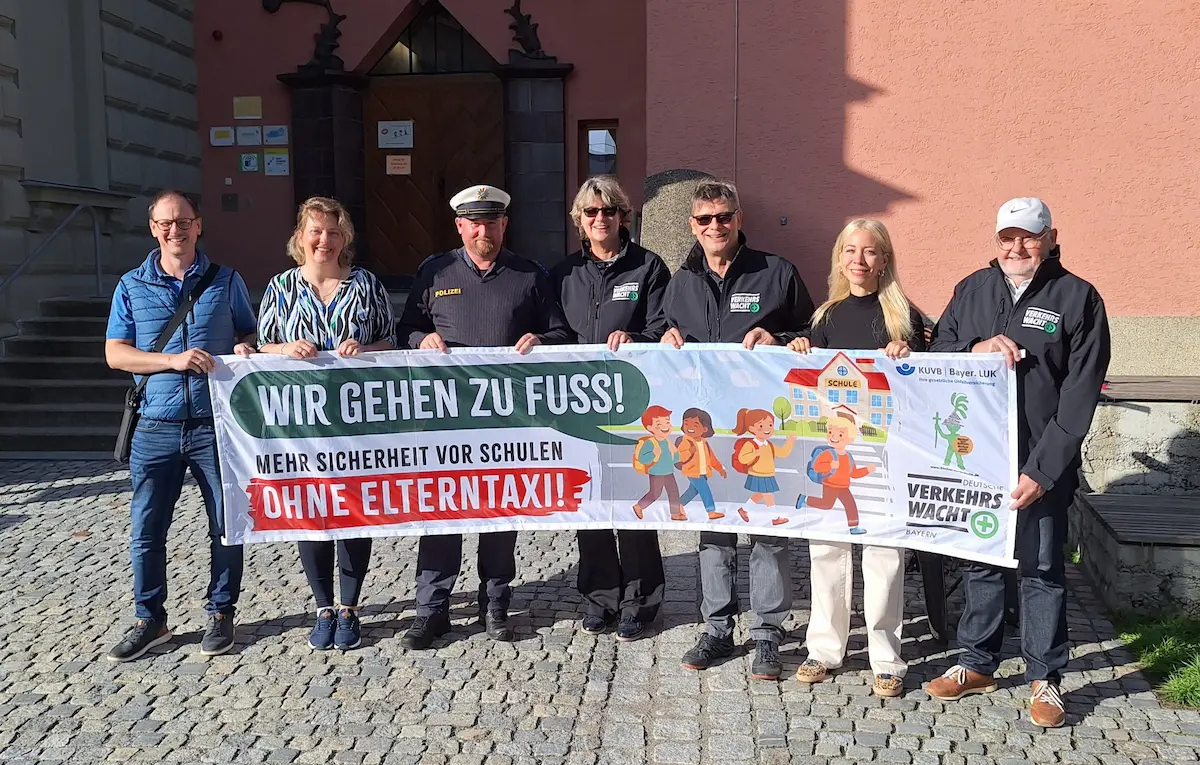 Mehrere Personen präsentieren vor der Grundschule St. Peter in Straubing ein Banner der Aktion „Wir gehen zu Fuß! Mehr Sicherheit vor Schulen ohne Elterntaxi“. Die Kampagne wirbt für sichere Schulwege und die eigenständige Mobilität von Schulkindern.